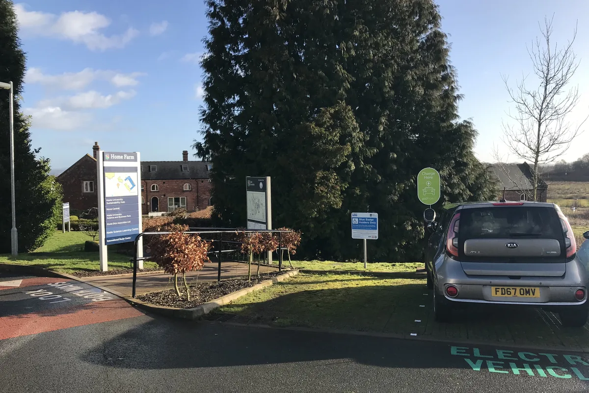 Electric car charging at a post in an outdoor car park, a typical route for an armoured power and Cat6A data cable feeding the charger