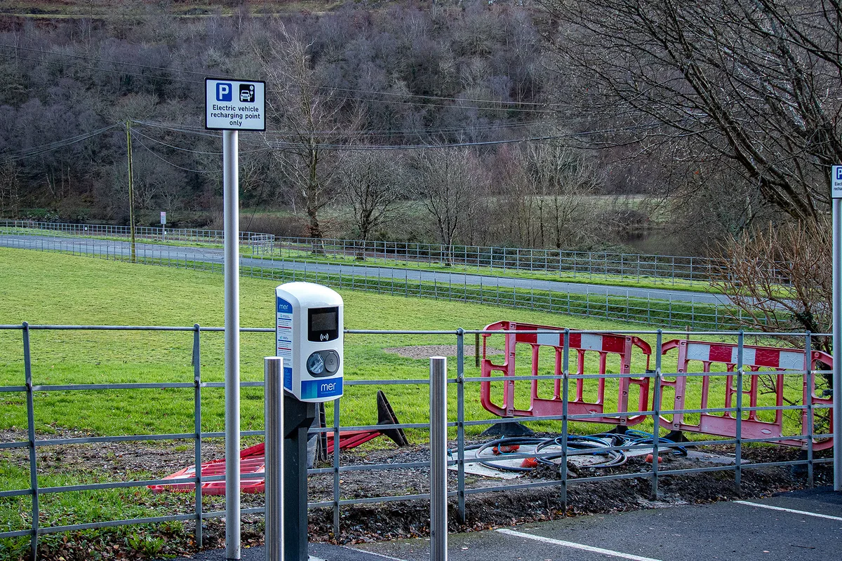 EV charge point being installed in a visitor car park behind safety barriers, where an armoured power and CAT5e data cable is laid to each post