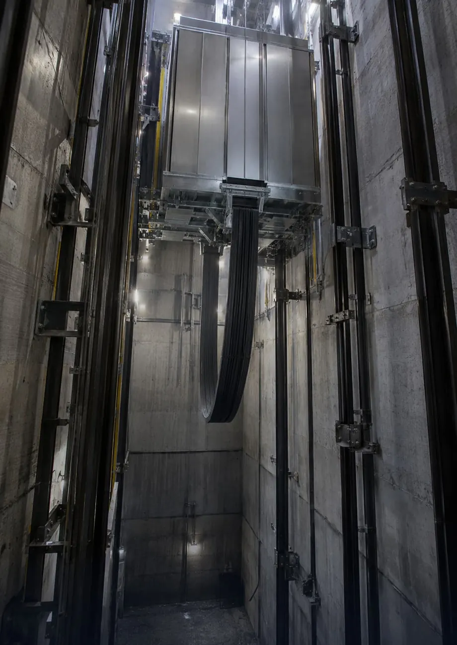 Flat travelling cable looping beneath an elevator car in a hoistway