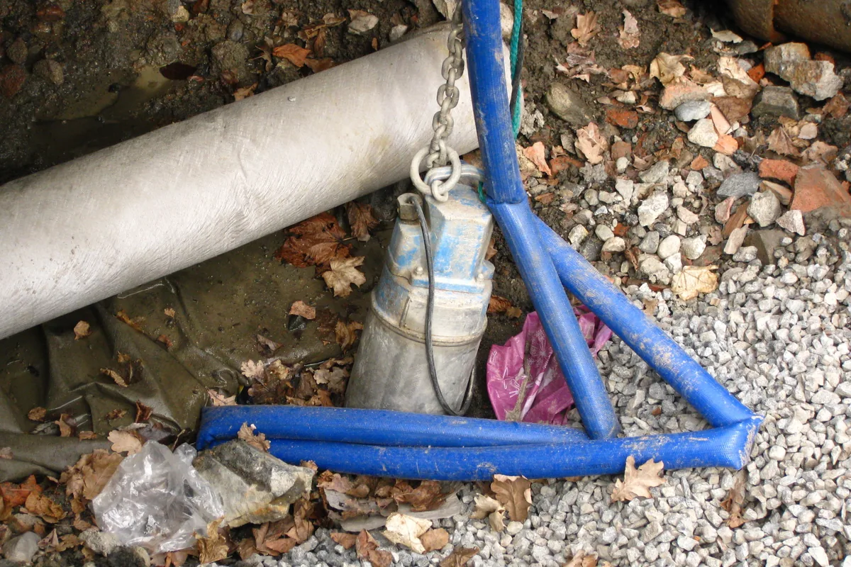 Submersible drainage pump standing in a gravel ditch on a lifting chain, with its power cable leading out of the water, the duty an ELCOSUB (N)TMH3S P2 cable is built for