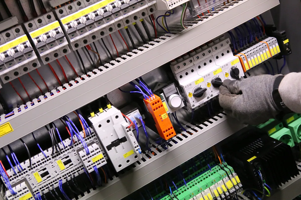 Inside an industrial control cabinet: circuit breakers, motor protection switches, relays and terminal blocks wired in cable ducts, where screened LiYCY control cables bring in field signals