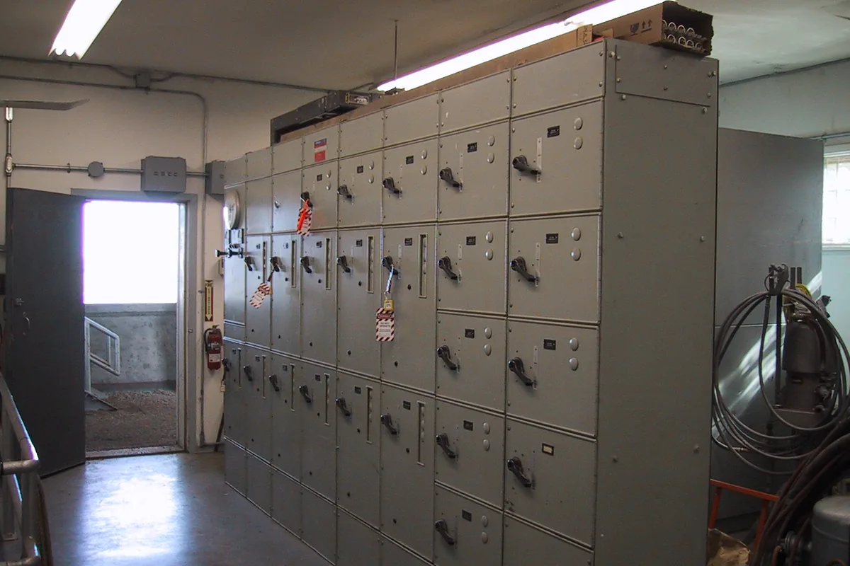 A row of grey 480 V motor control centre sections with starter-unit handles and lockout tags in a plant electrical room, equipment whose internal wiring uses 600 V PTFE wire such as UL 1198