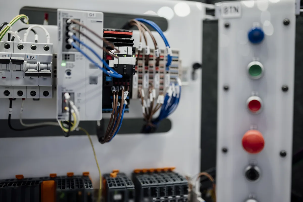 Close-up of a machine control panel with circuit breakers, PLC modules and terminal blocks connected by labelled hook-up wires, next to a column of push buttons, the kind of internal wiring done with UL 1213 PTFE hook-up wire