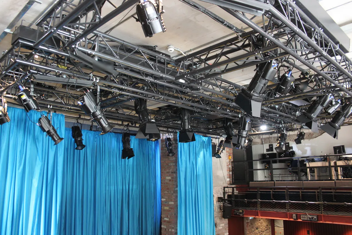 Studio theatre lighting rig with spotlights hung from black trusses above blue curtains, lighting lamps whose internal wiring uses 150 °C FEP wire such as UL 1333
