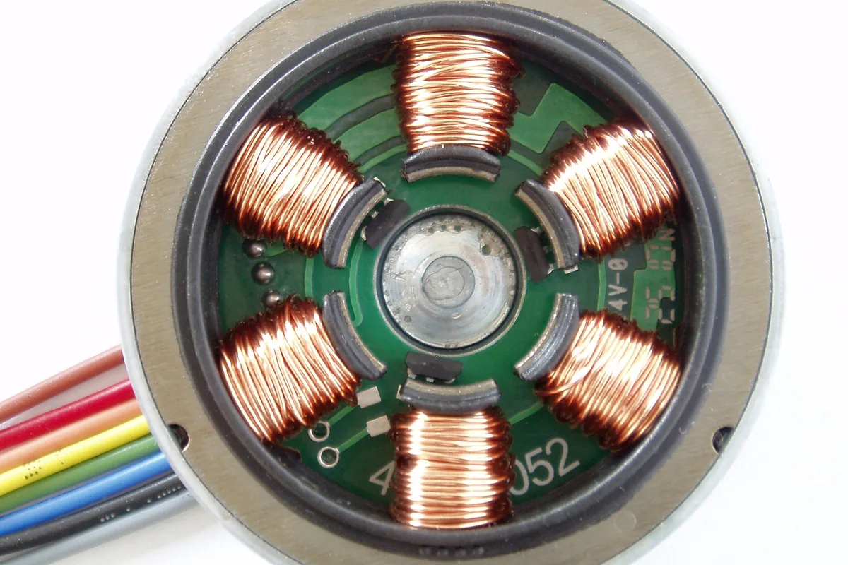 Stator of a small brushless DC motor with copper windings on a circuit board and a bundle of coloured lead wires leaving the housing, where lead wire connects a motor to its equipment