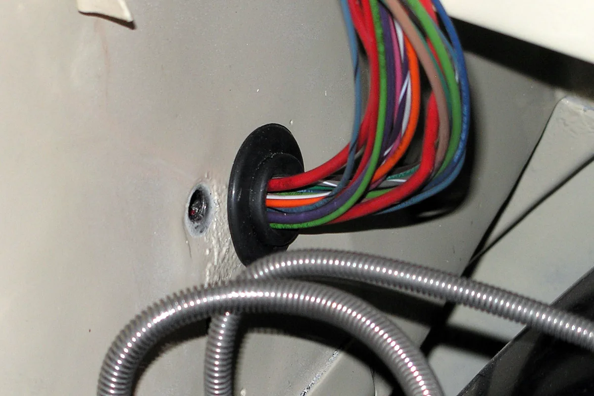 Bundle of coloured single-conductor leads passing through a rubber grommet into a vehicle engine compartment, a warm and crowded wiring run of the kind where 600 V, 125 °C UL 3173 XLPE wire is used