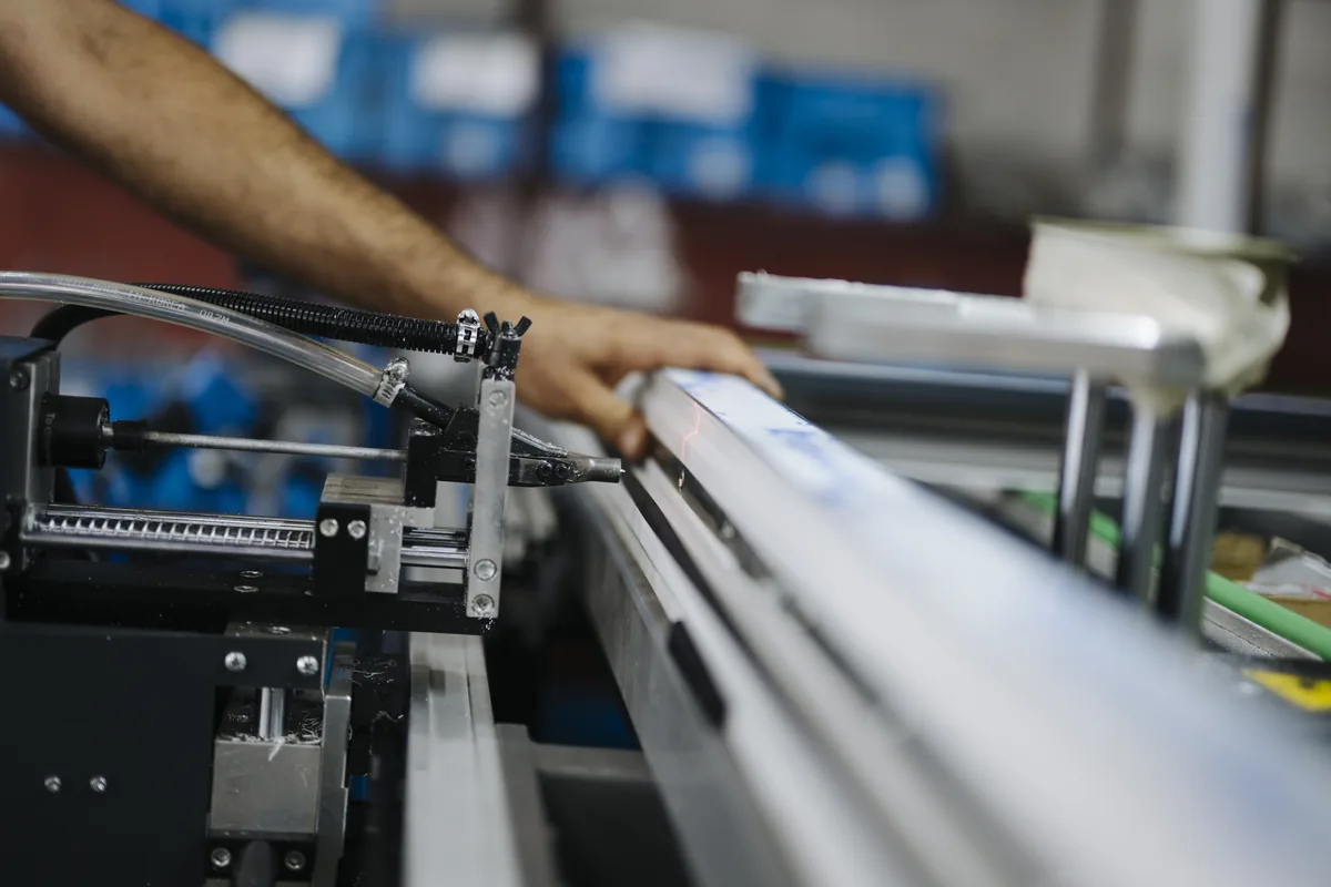 Operator feeding a metal profile into a production machine with exposed cable and hose routing, the kind of machine where steel-braided YSLYSY control cable is used